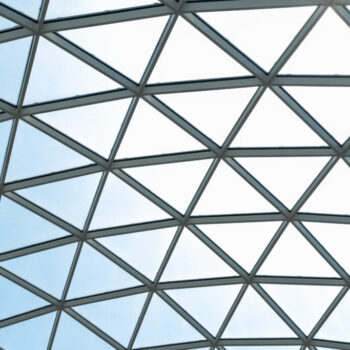 Architectural glass structure with a geometric triangular pattern on a blue sky background. Steel glass roof wall